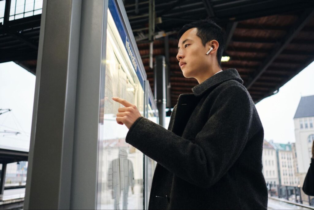 A man checking a train schedule display board at an outdoor station platform